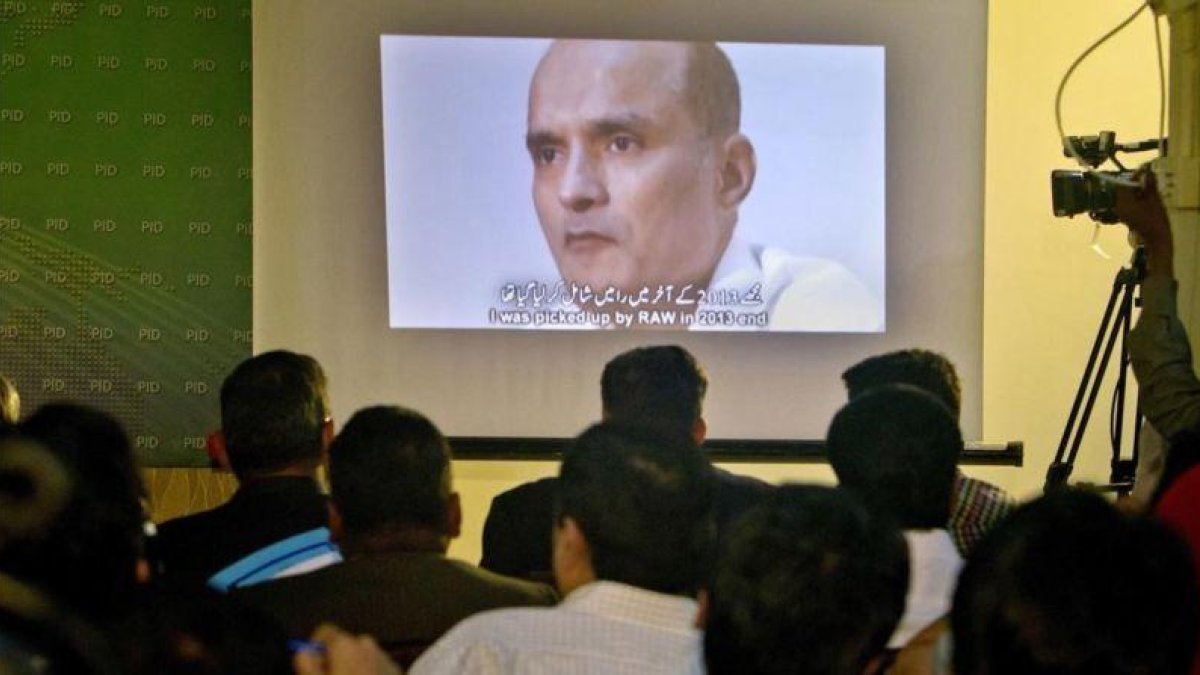 Unos periodistas observan la imagen de Jadhav mientras el portavoz del ejército paquistaní explcia su condena.-ANJUM NAVEED