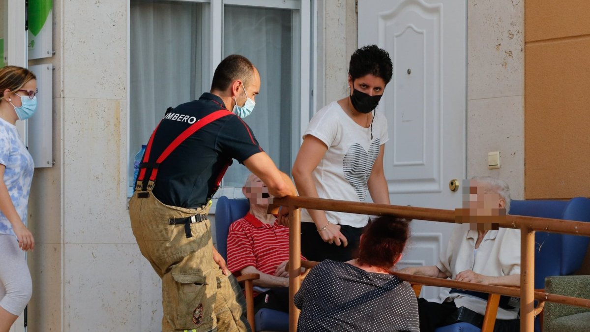 Varios residentes en el exterior del centro de mayores de Celada, asistidos por los bomberos y el personal sanitario. SANTI OTERO