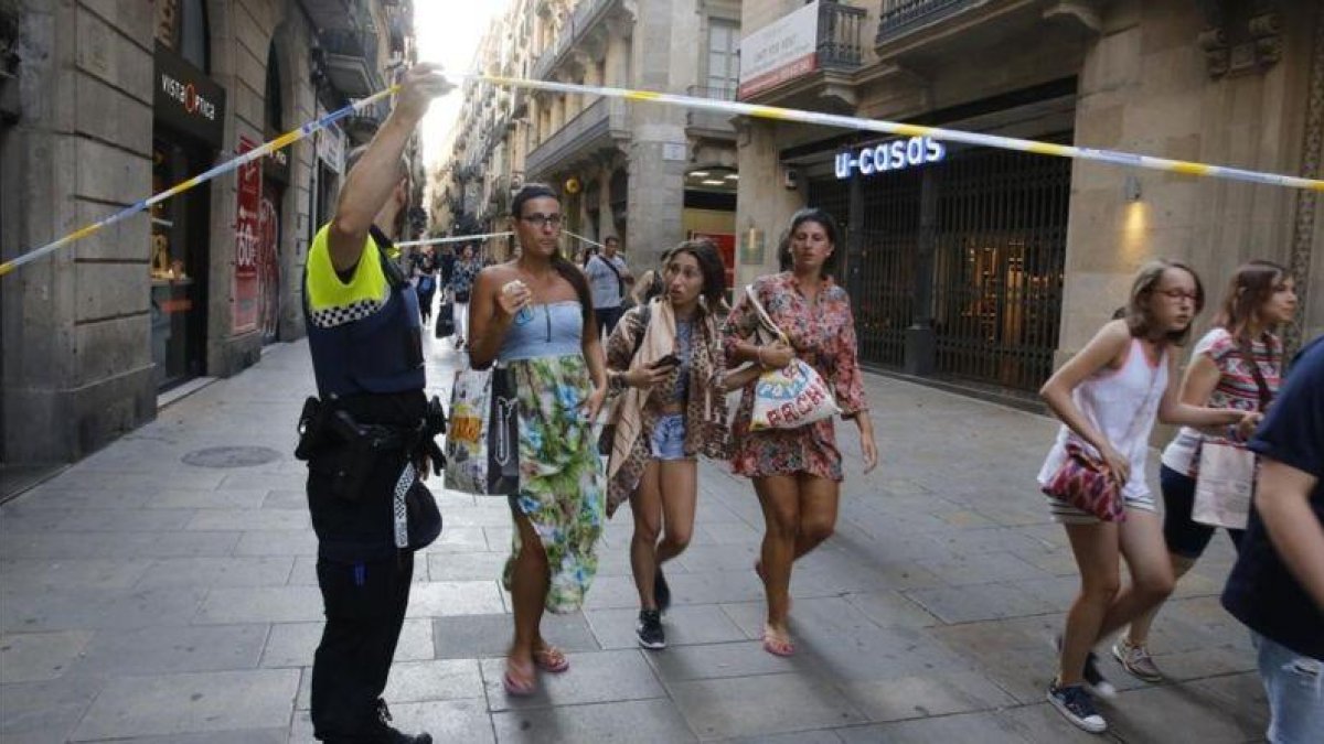 Unos turistas pasan bajo un cordón policial en la calle de Portaferrissa.-ÁLVARO MONGE
