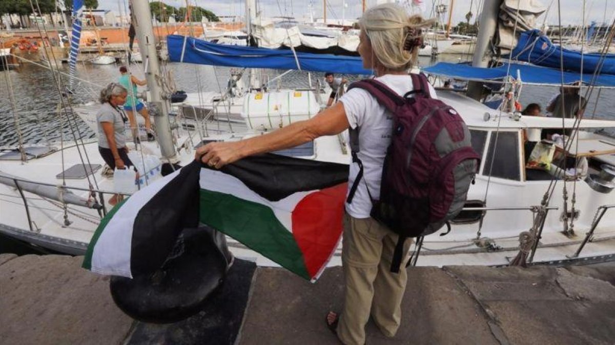 Una activista con la bandera palestina frente a uno de los dos veleros de la flotilla que ha partido hacia Gaza.-JULIO CARBÓ