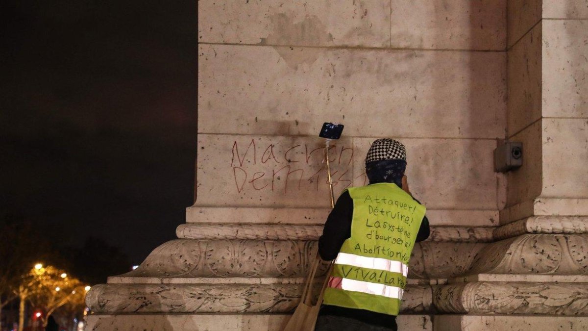 Anti-government protester scrawls graffiti that reads Macron resign on the wall of the Arc de Triumph in central Paris.-Zakaria ABDELKAFI AFP