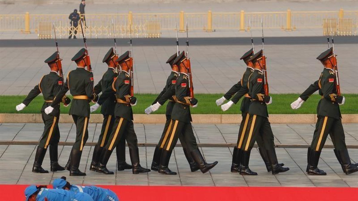 Dos trabajadoras limpian una alfombra roja ante un grupo de soldados, este lunes en Tiananmén.-EFE
