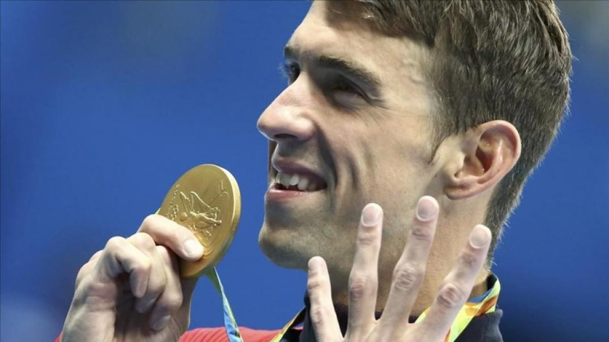 Phelps muestra su medalla señalando los cuatro oros que ha conseguido hasta ahora.-MICHAEL DALDER / REUTERS