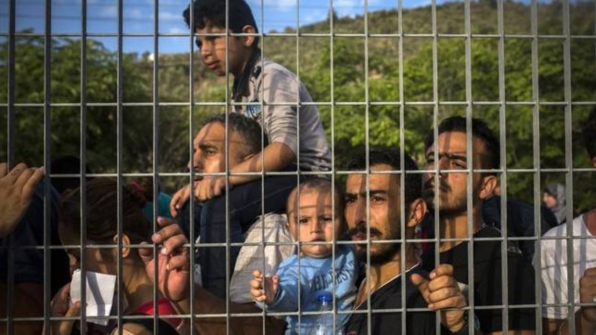 Refugiados e inmigrantes esperan tras una verja, en un campo de fútbol, a poder ser registrados, en Mitilene, este martes.-Foto: AP / SANTI PALACIOS