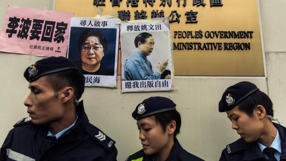 Unos policías frente a las fotos de Gui Minhai (izquierda) y otro de los cinco libreros, Yau Wentian, que fue condenado a 10 años de prisión en el 2015.-AFP / ANTHONY WALLACE