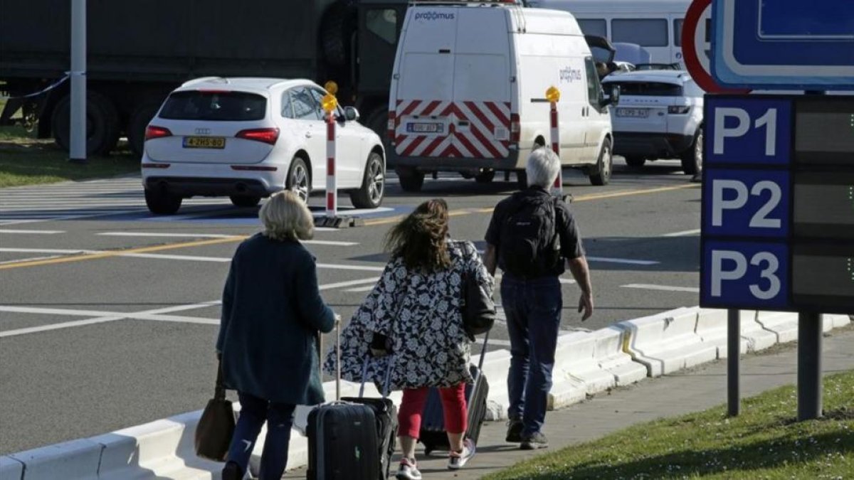 Varias personas caminan hacia la terminal mientras los vehículos hacen cola en un control de seguridad, en el aeropuerto de Zaventem, este lunes.-AFP / THIERRY ROGE