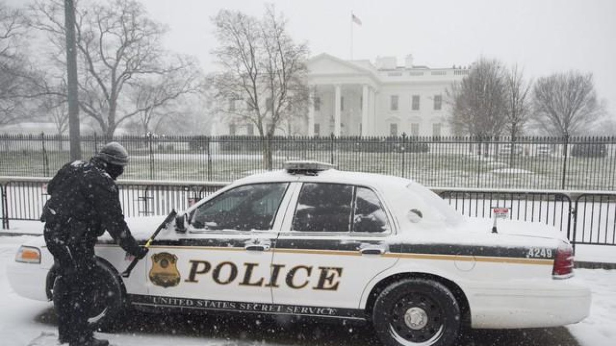 Un miembro del servicio secreto limpia la nieve de un vehículo en la Avenida Pennyslvania.-EFE/ JIM LO SCALZO