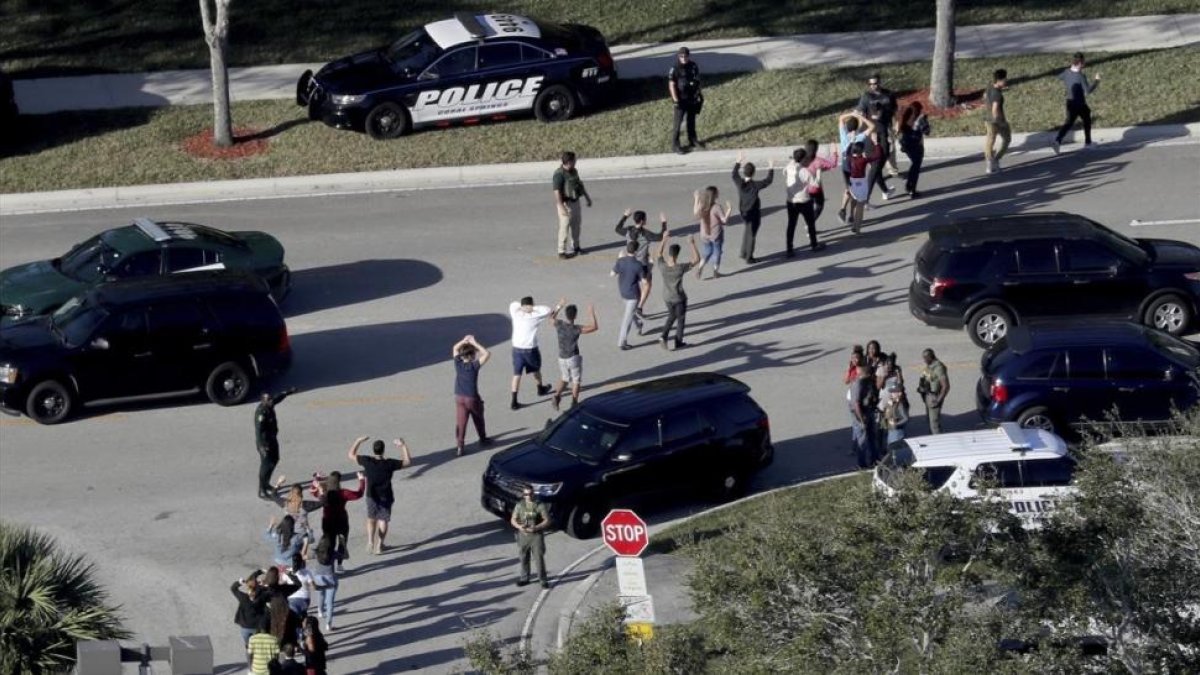 Evacuación de estudiantes con los brazos en alto a la salida del instituto Marjory Stoneman Douglas, en Parkland (Florida), el 14 de febrero.-/ AP / MIKE STOCKER