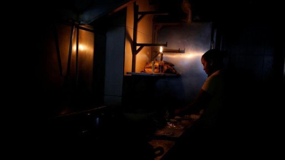 Una mujer usa la luz de una linterna para trabajar en la cocina de un restaurante tras un nuevo apagón en Caracas.-CARLOS GARCÍA RAWLINS (REUTERS)