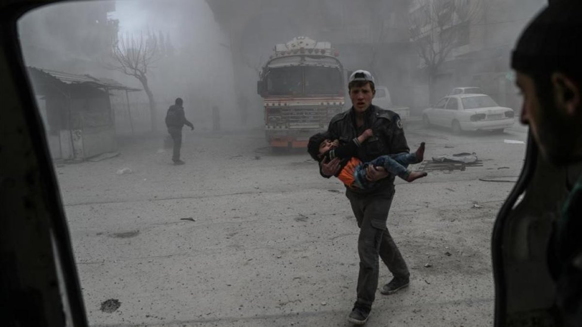 Un voluntario de los Cascos Blancos sirios lleva a un niño herido en brazos hasta una ambulancia, tras un bombardeo en Duma (Guta Oriental), el 22 de febrero.-/ EFE / MOHAMMED BADRA