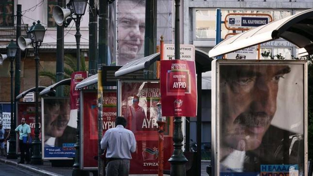 Un hombre pasa junto a un cartel electoral de Meïmarakis (derecha) y otro de Tsipras (arriba), este miércoles en Atenas.-AFP/LOUISA GOULIAMAKI