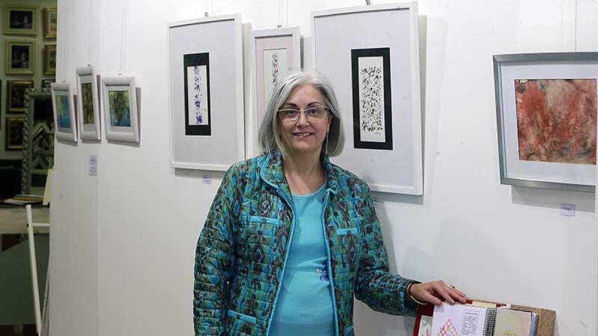 Carmen Palacín, junto a una parte de la muestra y con los cuadros de su sobrino Pablo al fondo.-Raúl Ochoa