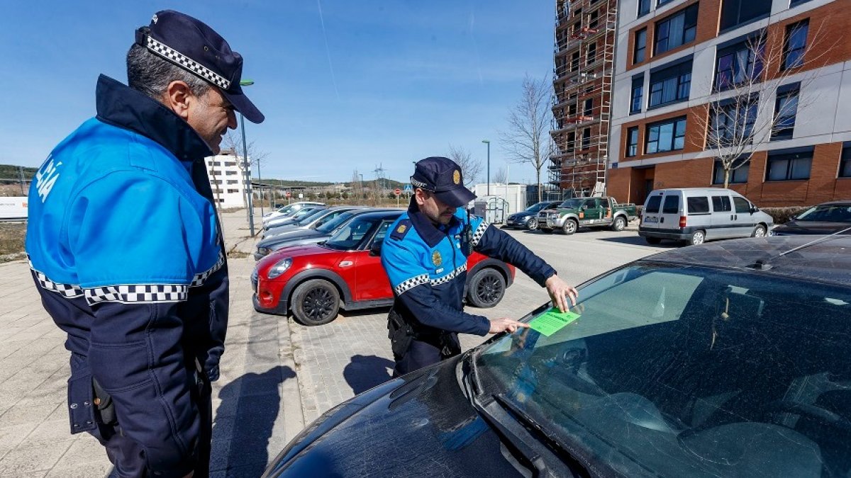 Dos agentes de la Policía Local de Burgos colocan una pegatina verde en un coche que podría estar abandonado. SANTI OTERO