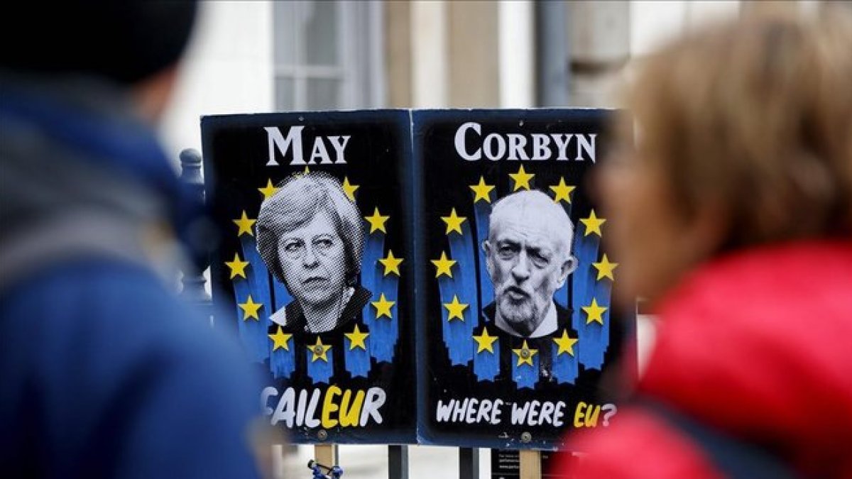 Unos peatones pasan junto a carteles con la primera ministra británica, Theresa May, y el líder del Partido Laborista, Jeremy Corbyn, cerca del Parlamento, en Londres.-TOLGA AKMEN (AFP)