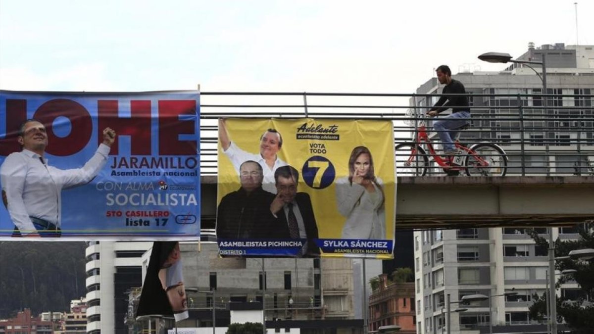 Ciudadanos caminan frente a varios carteles electorales en Quito.-EFE / JOSÉ JACOME