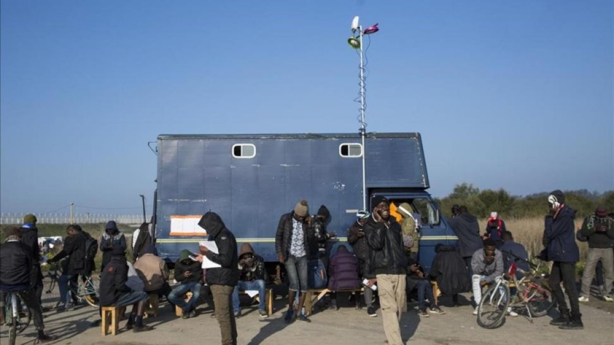 Inmigrantes del campamento francés de Calais usan teléfonos móviles junto a un camión que ofrece conectividad.-JACK TAYLOR