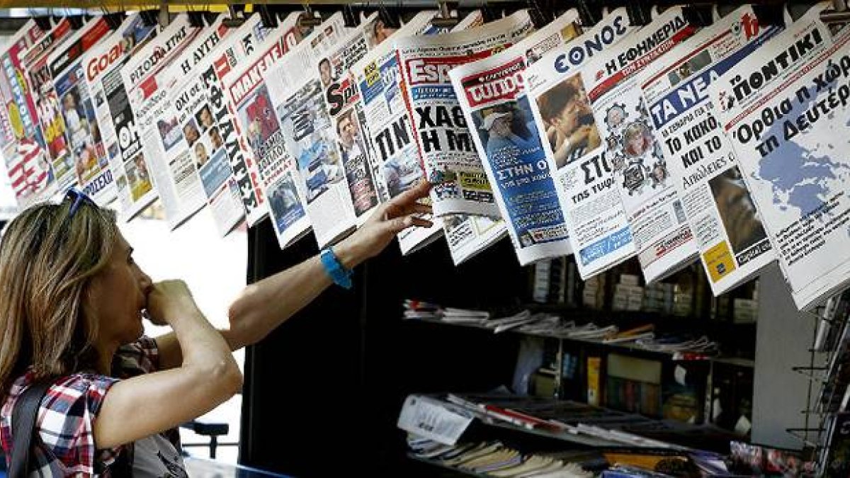 Una mujer mira con curiosidad y cierto temor la oferta informativa de la prensa griega.-Foto: AP / PETROS KRADJIAS