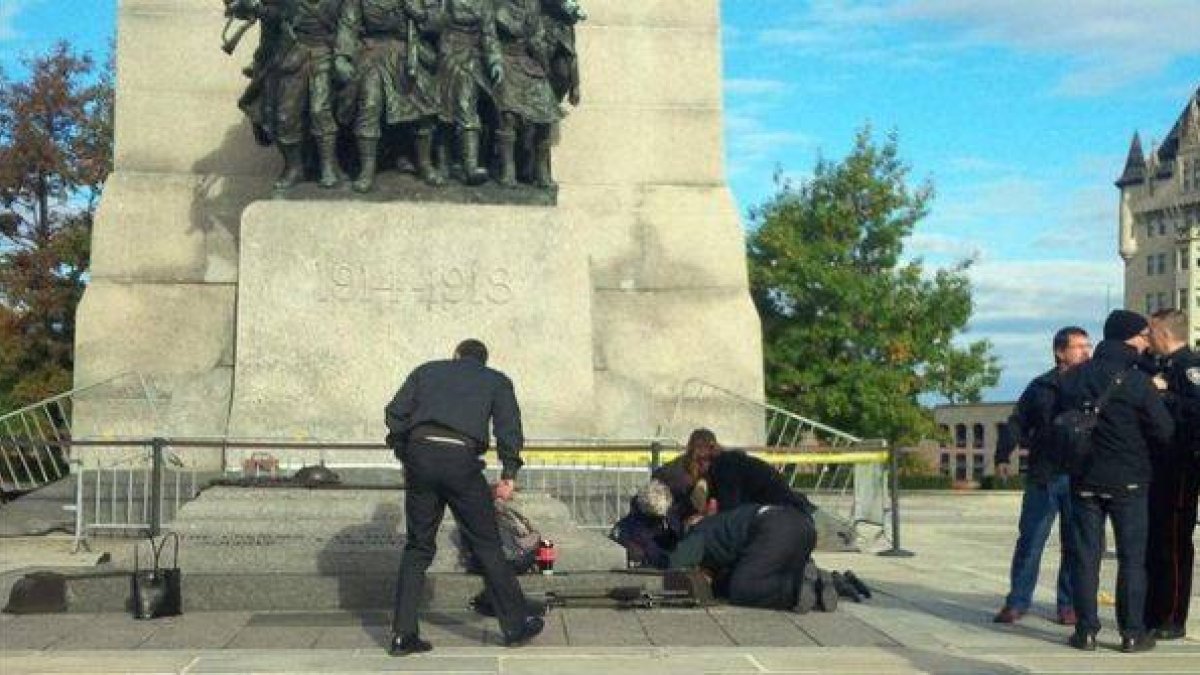 Unos soldados atienden a un compañero herido, ante el monumento de los veteranos de guerra en Ottawa.-Foto: EL PERIÓDICO