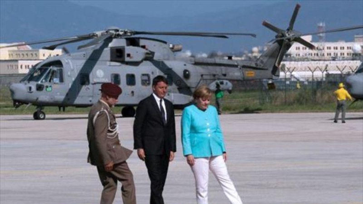 Renzi, Merkel y un oficial tratan de ajustar la alfombra roja en el aeropuerto de Nápoles, antes de desplazarse a Ventotene.-AFP / MARIO LAPORTA