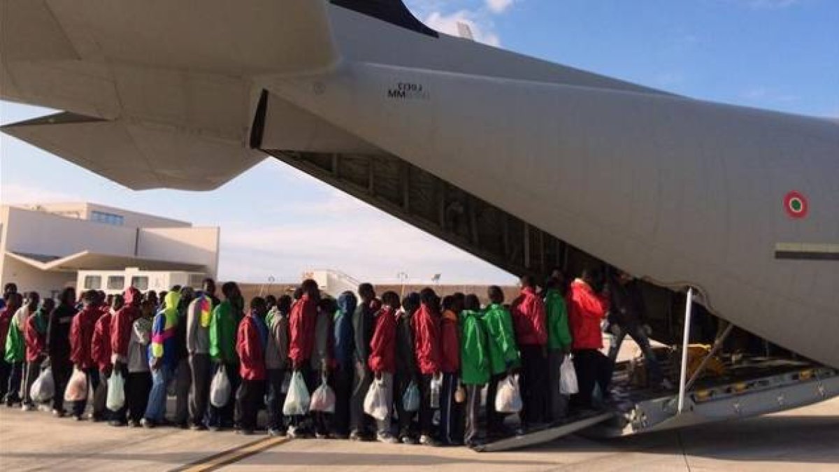 Inmigrantes subsaharianos hacen cola antes de subir a un avión militar que les trasladará a la península italiana, este lunes, en Lampedusa.-