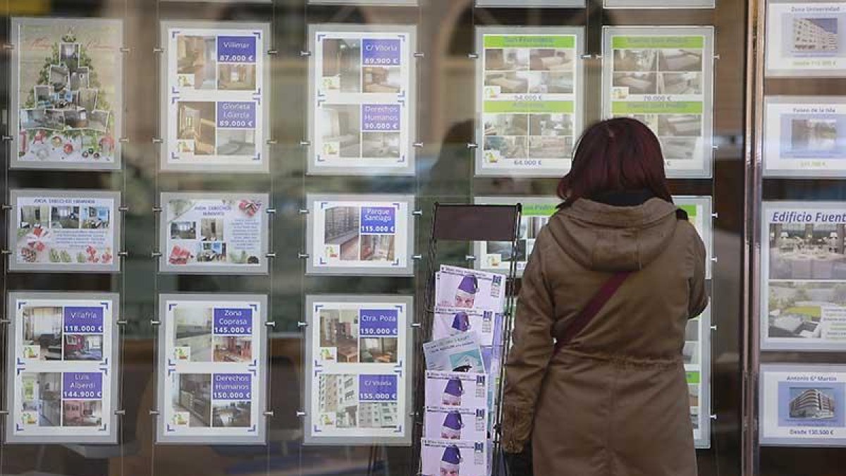 Una mujer contempla los precios de venta de viviendas en el escaparate de una inmobiliaria.