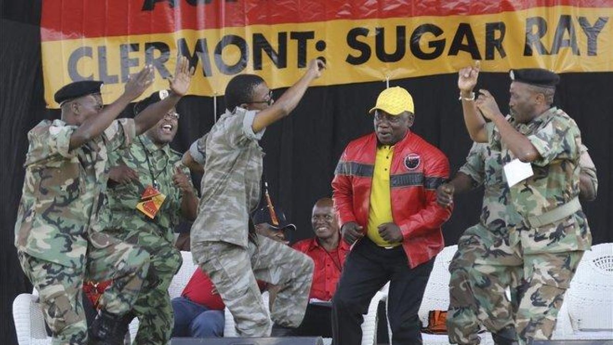 El presidente sudafricano y líder del Congreso Nacional Africano, Cyril Ramaphosa (con chaqueta roja) baila con unos militares durante un mitin de su partido en la ciudad de Durban.-ANTOINE CHAUVEL (AP)