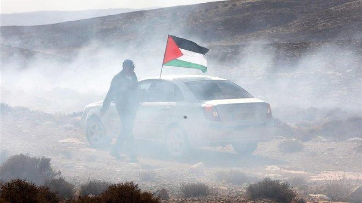Un hombre ondea la bandera palestina entre gas lacrimógeno, este domingo durante una protesta en el pueblo cisjordano de Shiyoukh, cercano a Hebrón.-ABED AL HASHLAMOUN (EFE)