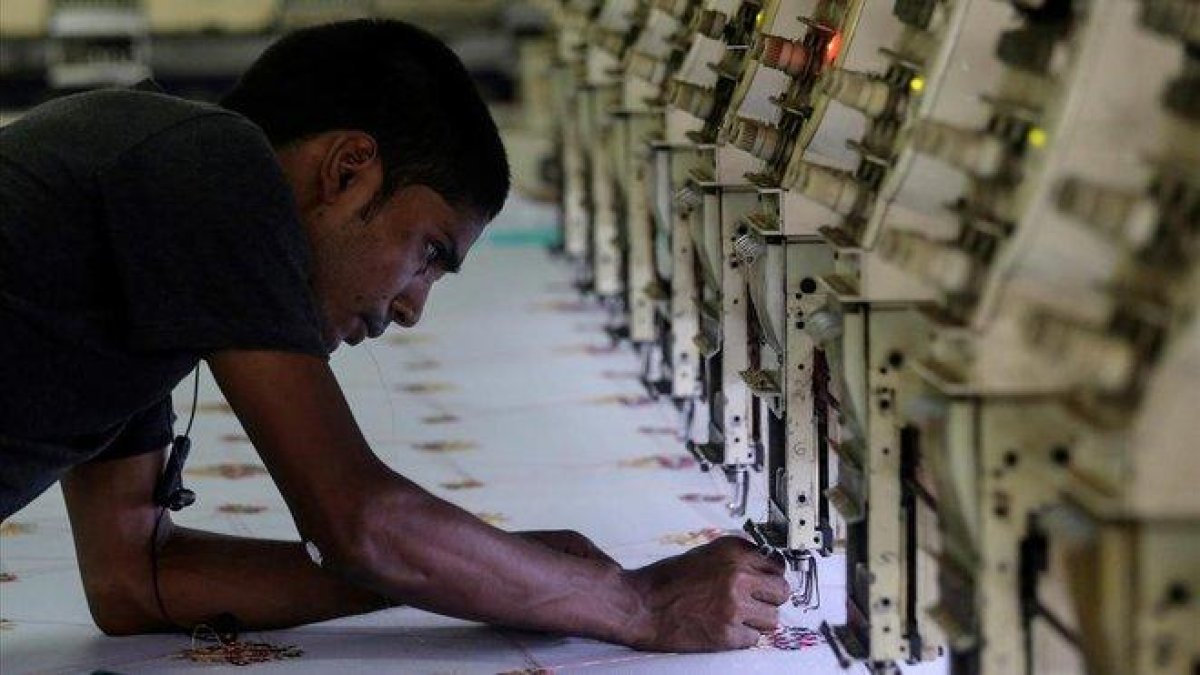 Un trabajador indio ajusta una máquina de coser en un planta de Bombai (India).-