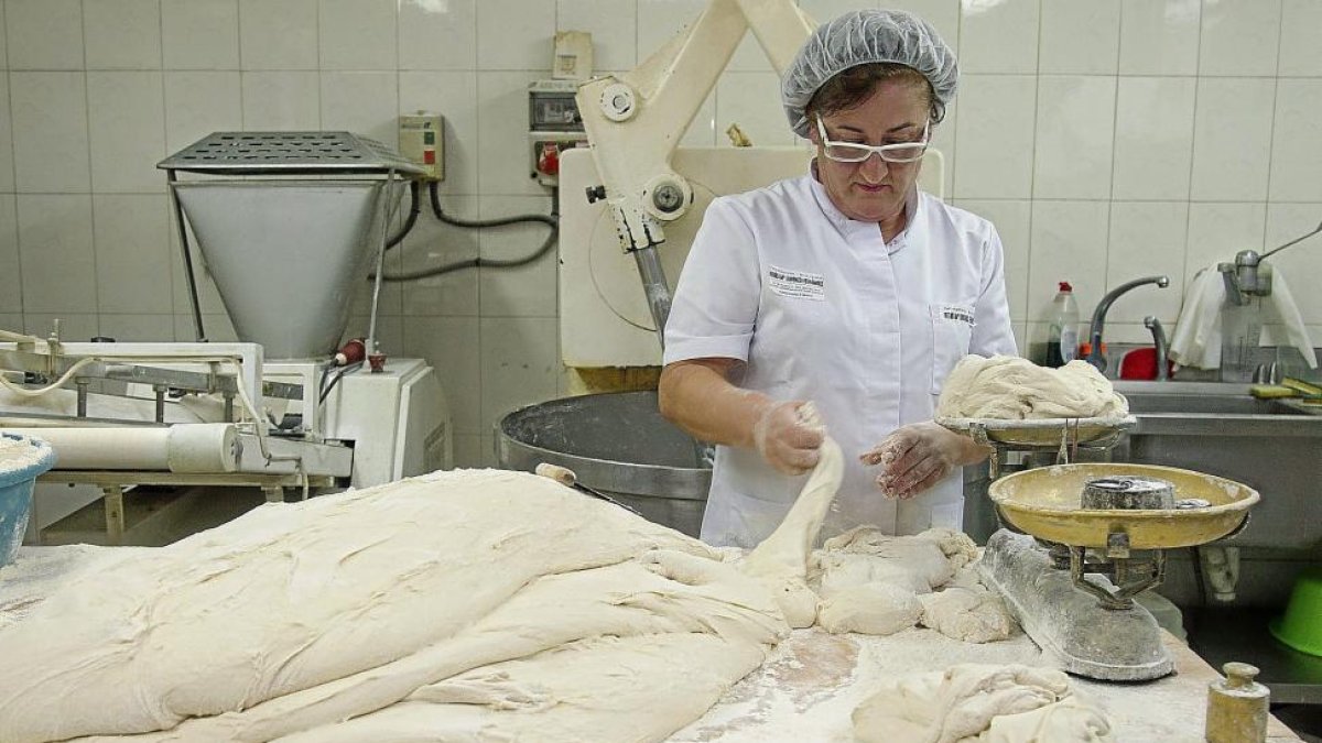 Encarna Terrón corta porciones de masa, que pesa en una balanza tradicional, en la panadería de Carbajales de Alba (Zamora).-MIRIAM DENEIVA