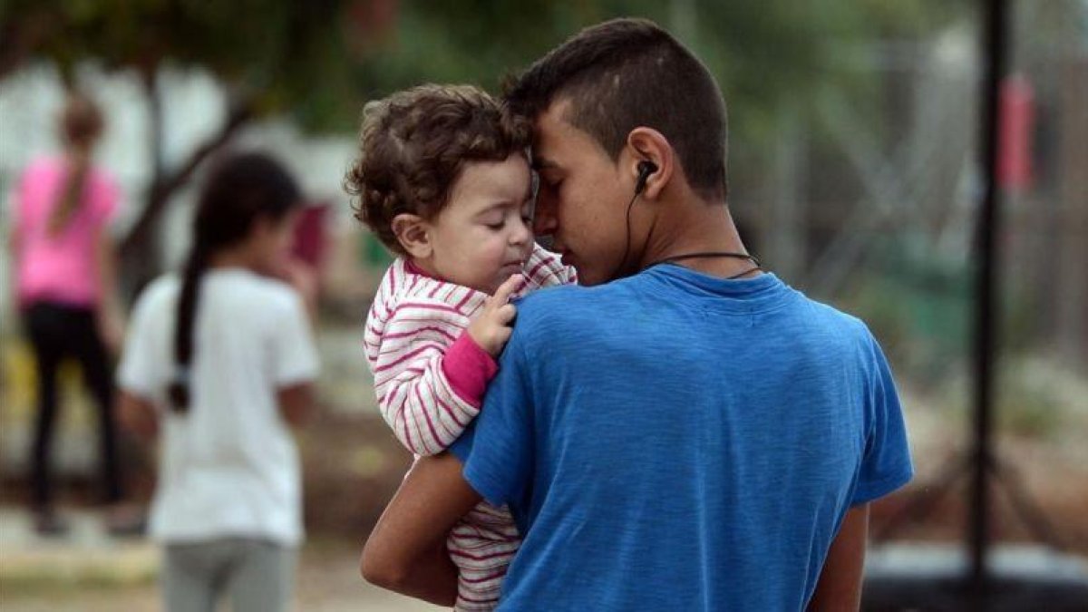 Un chico sostiene en brazos a su hermano pequeño en el campo de refugiados de Kara Tepe, donde algunos fueron trasladados tras un incendio en el de Moria, en Lesbos (Grecia), el 21 de septiembre.-AFP / LOUISA GOULIAMAKI