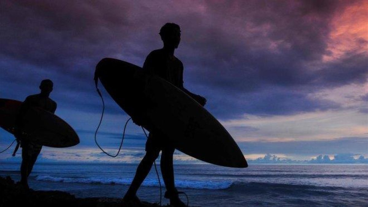 Jóvenes indonesios caminan con sus tablas de surf en una playa de Aceh, en la isla de Sumatra.-