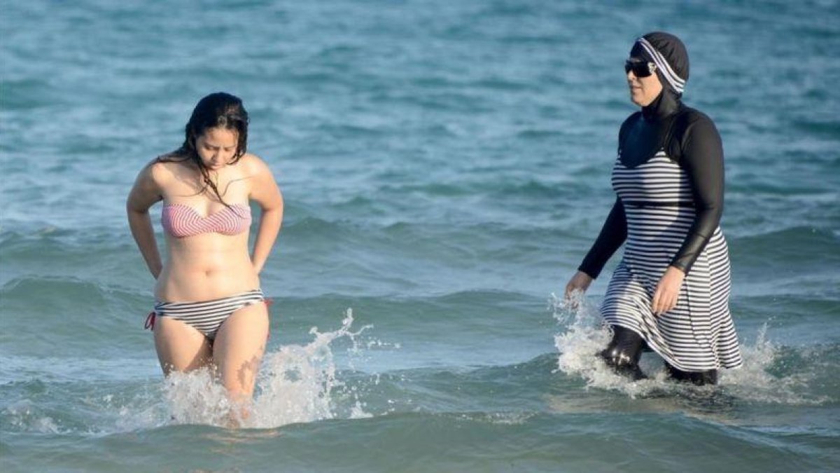 Una mujer con biquini y otra con 'burkini' en la playa tunecina de Ghar El Melh.-AFP / FETHI BELAID