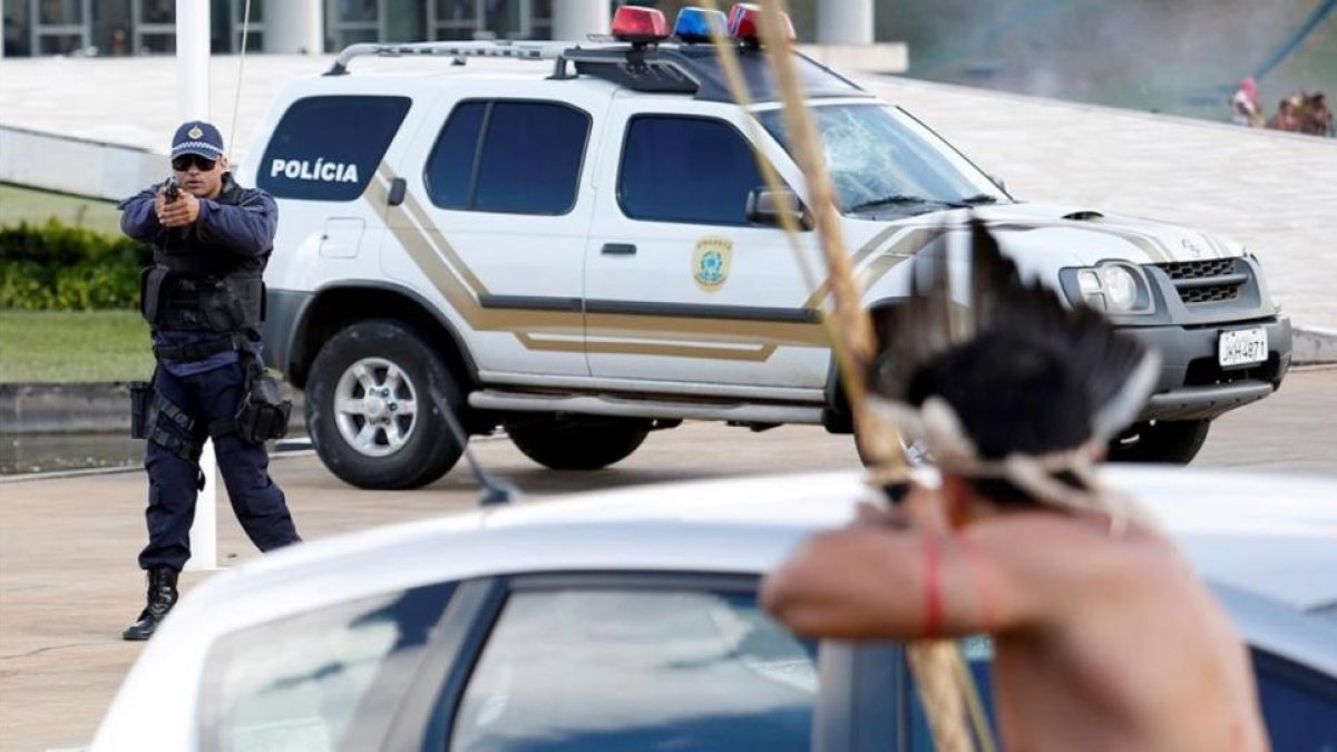 Un policía apunta con su arma a un indígena armado con un arco y flechas frente al Congreso de Brasilia.-REUTERS / GREGG NEWTON
