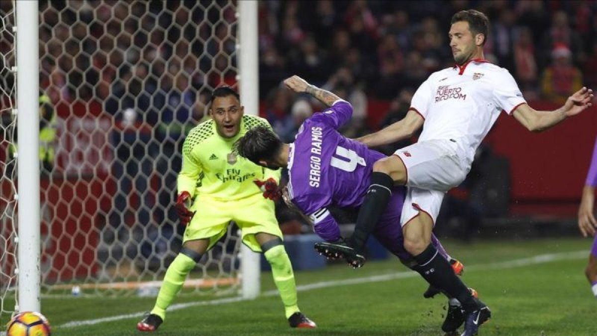 Keylor Navas observa el despeje de Sergio Ramos ante el sevillista Franco Vázquez.-EFE / JULIO MUÑOZ