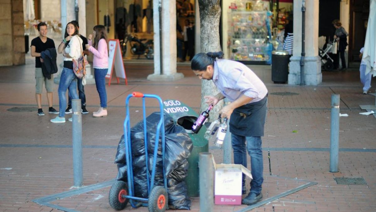 Una persona echa varias botellas de cristal en un contenedor de vidrio.-ISRAEL L. MURILLO