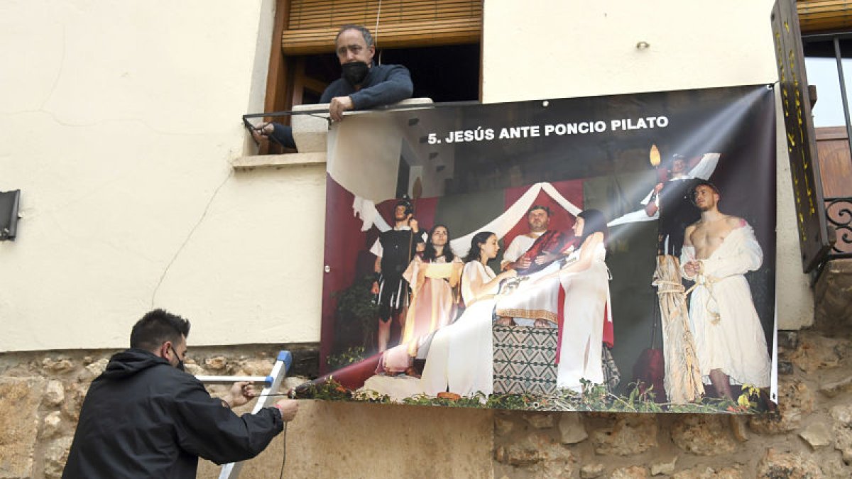 Dos personas colocan una de las lonas con las fotos de la Semana Santa de Covarrubias. ICAL