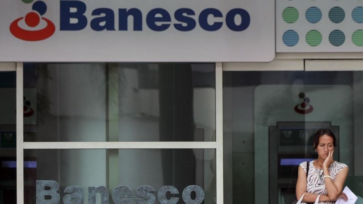 Una mujer espera frente a una oficina del banco Banesco en Caracas.-/ AFP / LUIS ROBAYO