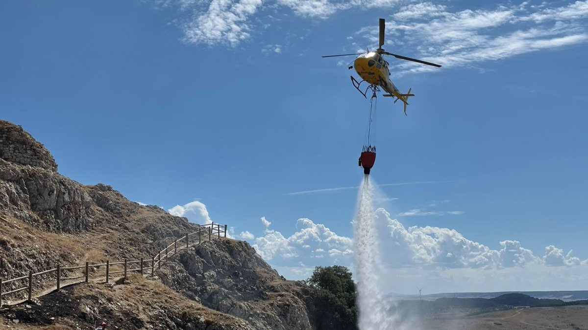 Un helicóptero echa agua sobre la ladera del castillo de Monasterio de Rodilla. ECB