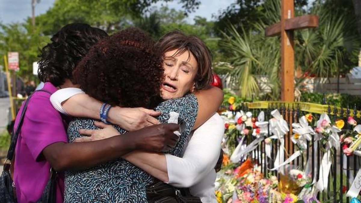 Tres mujeres se abrazan junto a la ofrenda floral frente a la iglesia metodista, en Charleston, este sábado.-Foto:   AP / CURTIS COMPTON