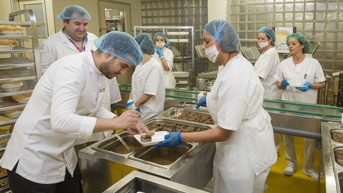 El chef Ricardo Temiño (en primer plano) coloca el lechazo en un plato ante la mirada del jefe de cocina del HUBU, Víctor Hernando y de un grupo de trabajadoras de la cocina del hospital.-ISRAEL L. MURILLO