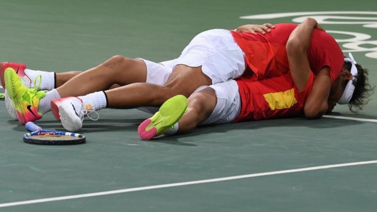 Rafa Nadal y Marc López se abrazan en el suelo tras clasificarse para la final olímpica.-AFP / LUIS ACOSTA