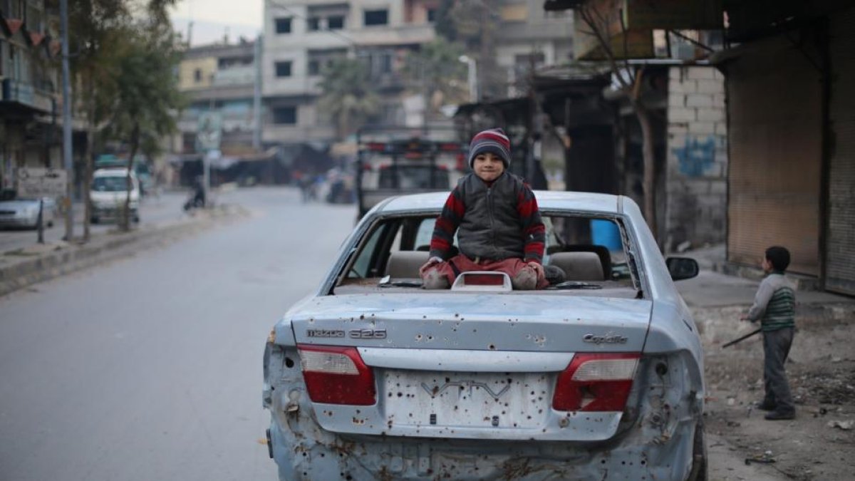 Un niño sirio sentado sobre un coche dañado por las explosiones del este de Ghouta.-AMER ALMOHIBANY