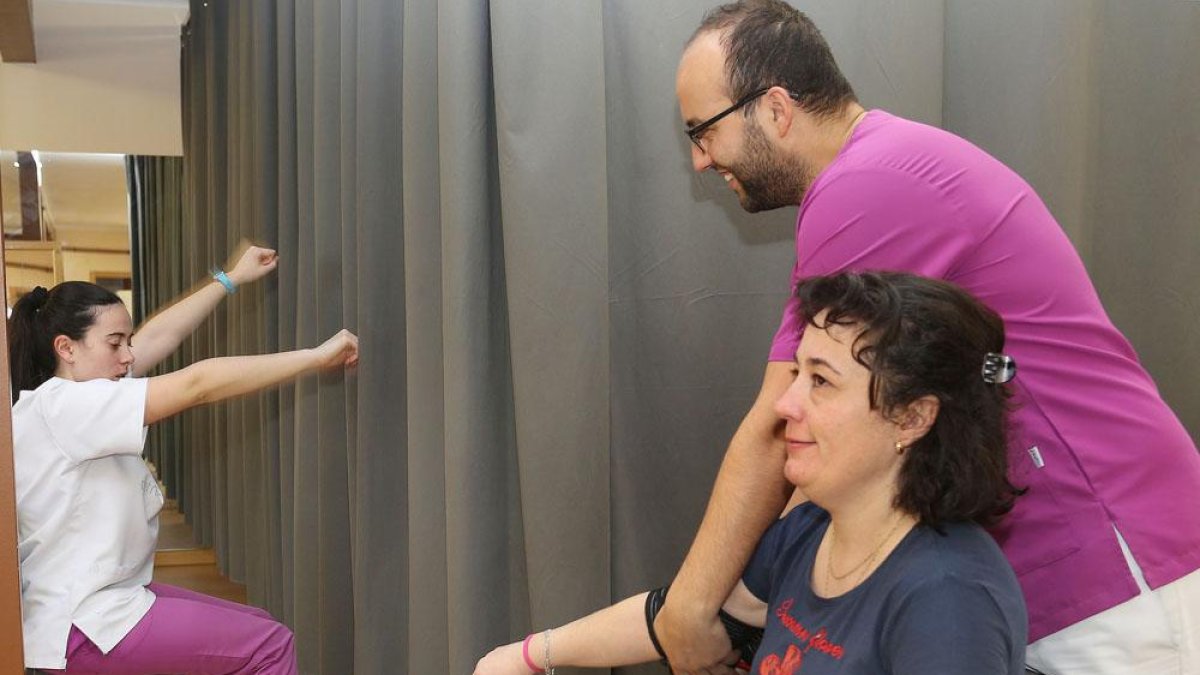 Un fisioterapeuta asite a una usuaria que realiza ejercicios de rehabilitación.-ICAL