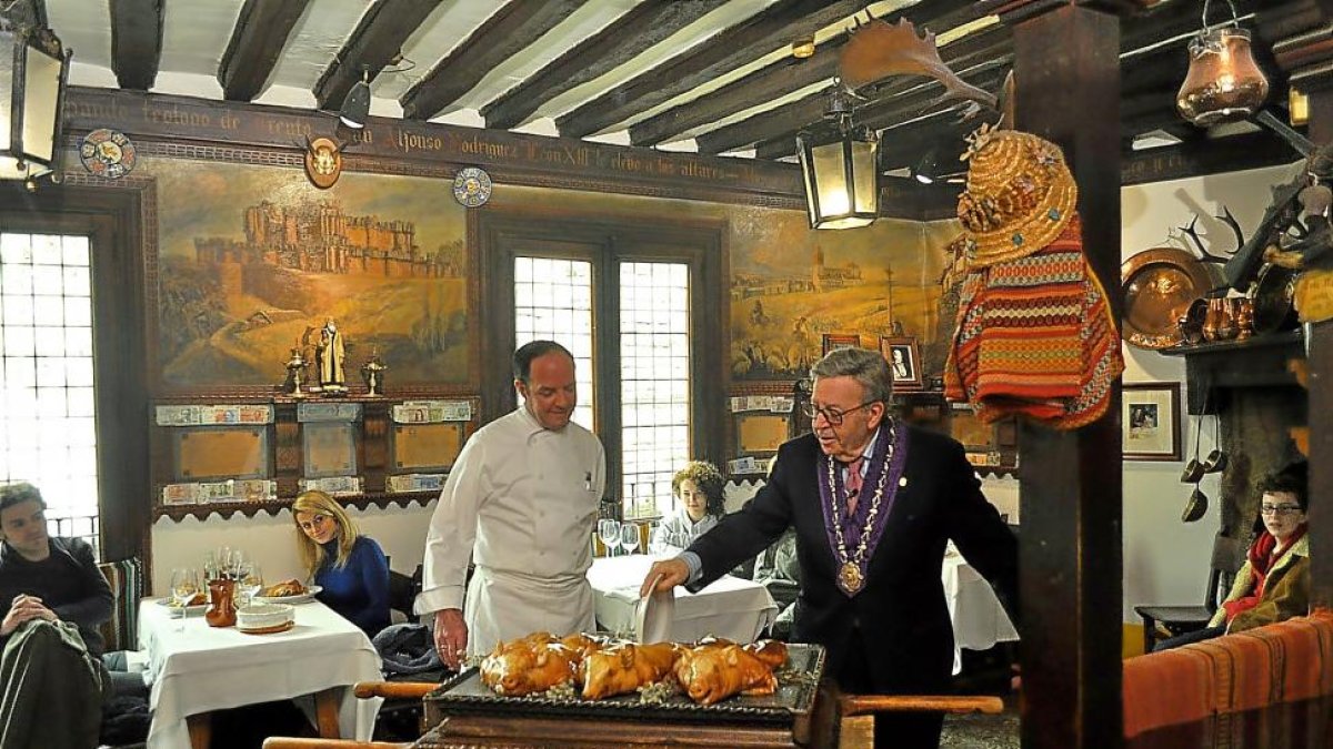 Alberto López (d) y su hijoCándido trinchan un cochinillo en una sala del mesón.-I. M.