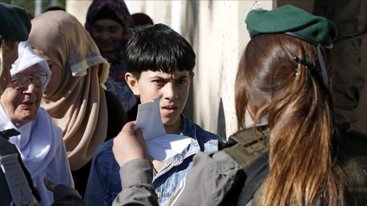 Un nino palestino muestra su carnet de identidad a una agente israelí mientras espera para poder cruzar a Jerusalen a través del puesto de control de Belén.-ABED AL HASHLAMOUN