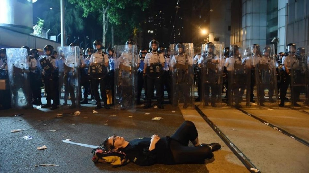Una manifestante estirada en el suelo bloquea una de las calles de Hong Kong frente a una fila de policías.-AFP / ANTHONY WALLACE