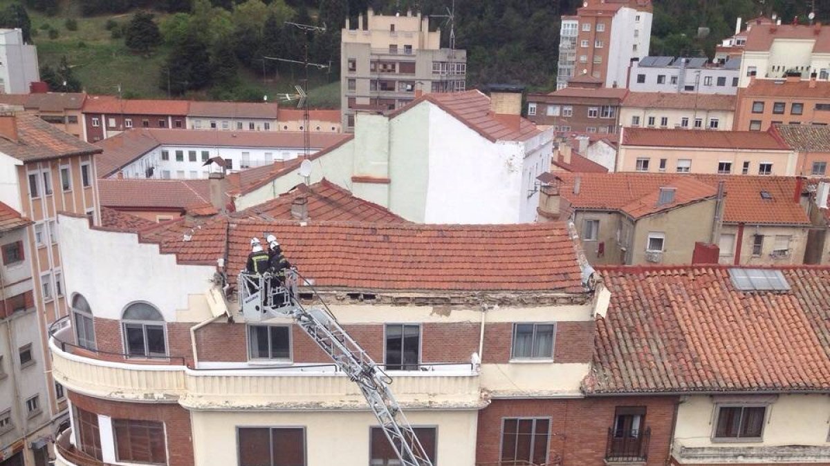Los bomberos actúan en la cornisa, con parte de los cascotes sobre la acera.-ISRAEL L. MURILLO