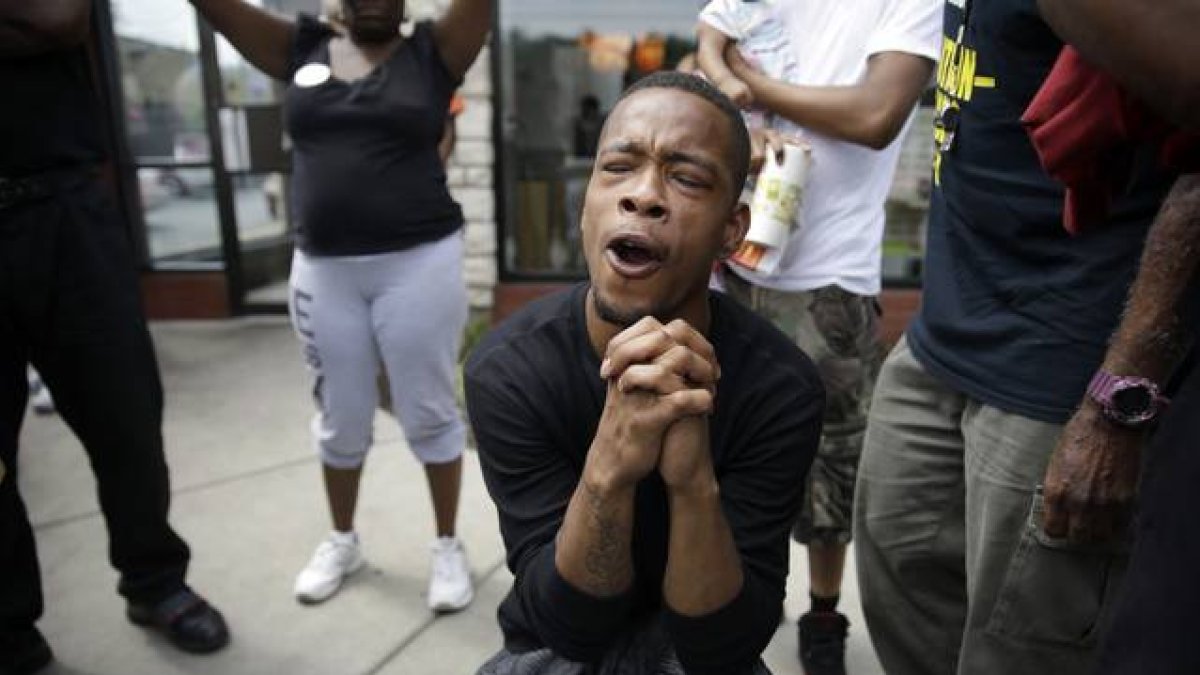 Un hombre reza mientras la policía dispersa a los manifestantes en Ferguson tras el asesinato de Michael Brown.-Foto: AP / Jeff Roberson