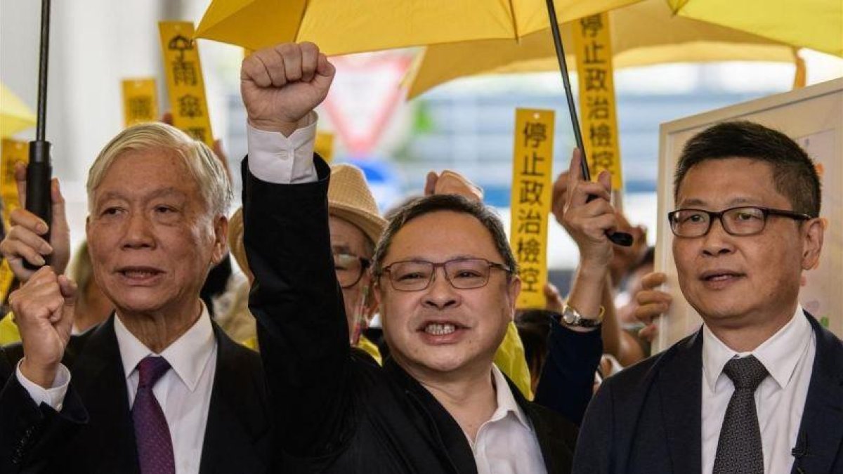 De izquieda a derecha, Chu Yiu-ming, Benny Tai y Chan Kin-man, saludan a su seguidores antes de entrar en el tribunal de West Kowloon en Hong Kong.-AFP / ANTHONY WALLACE