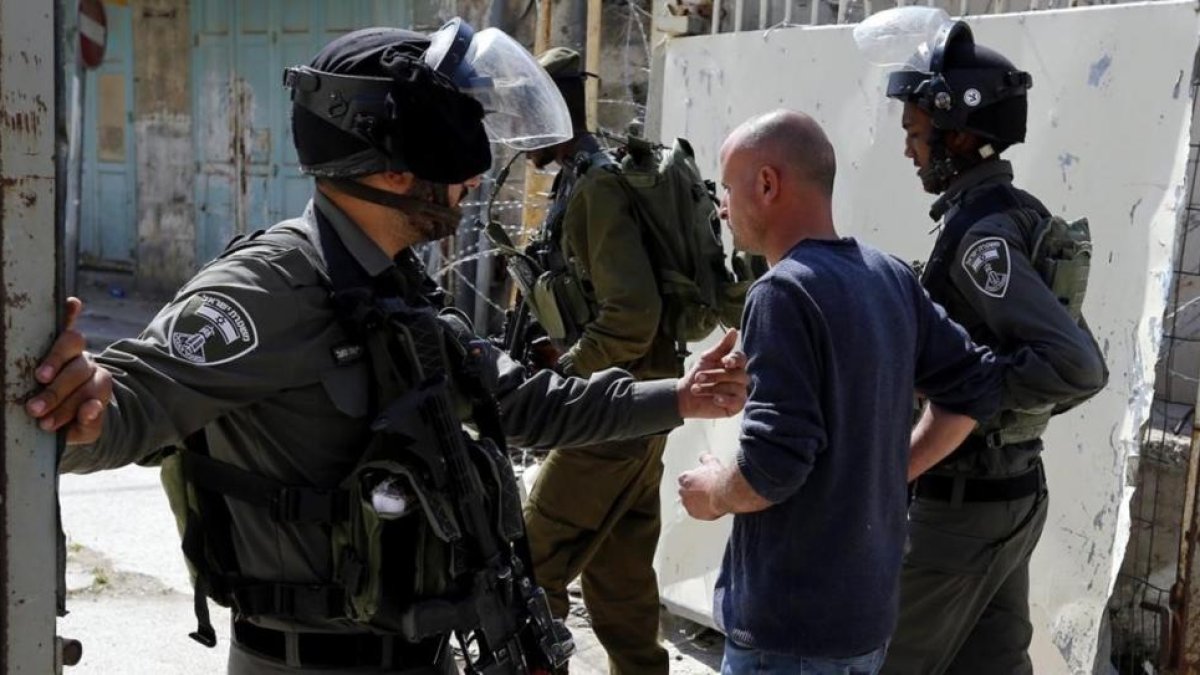 Soldados israelies arrestan a un joven palestino durante una protesta en la ciudad cisjordana de Hebron ayer lunes 17 de abril.-EFE / ABED AL HASHLAMOUN